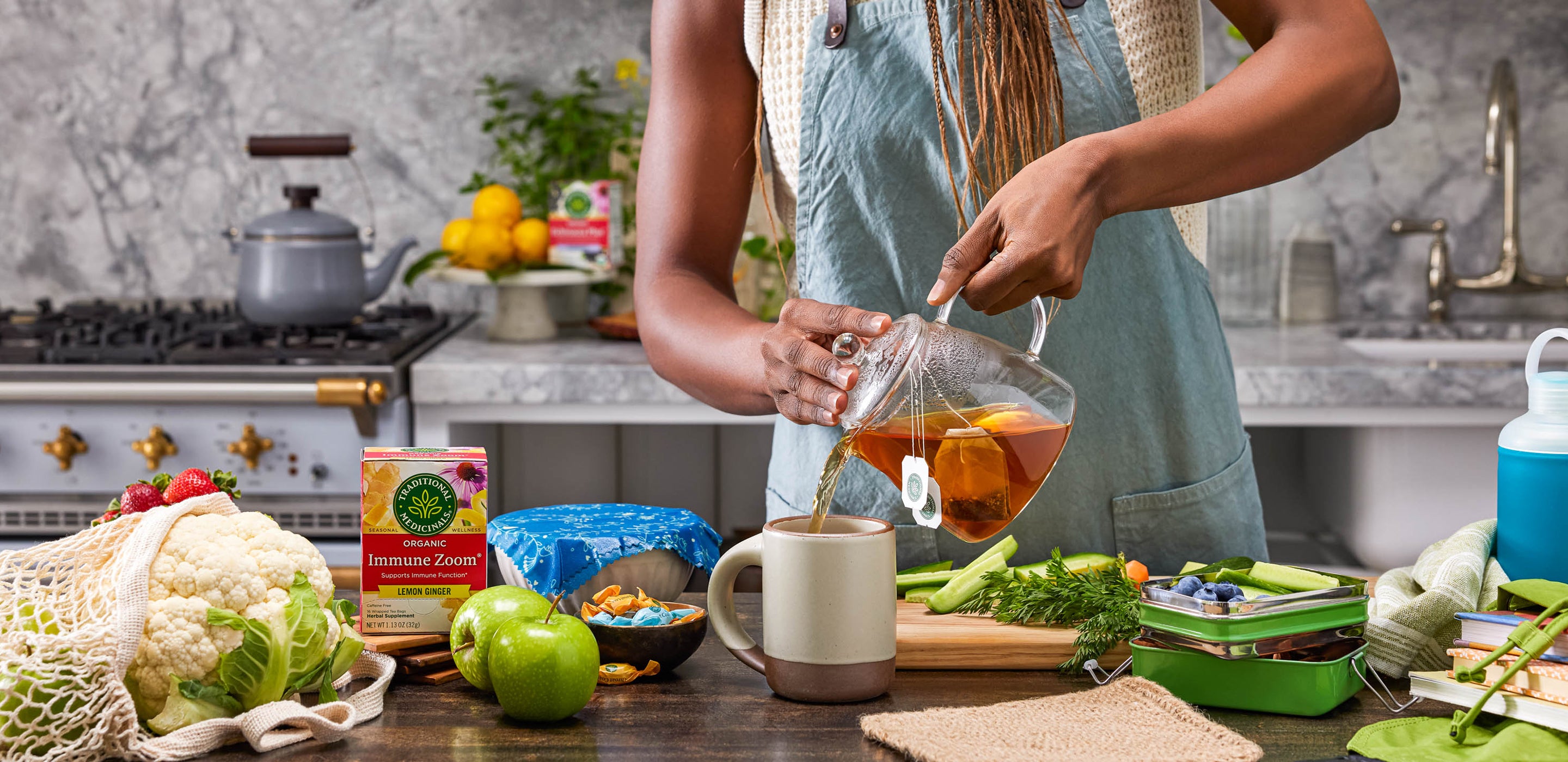 Mother packing school lunch with tea, fruits and veggies in kitchen