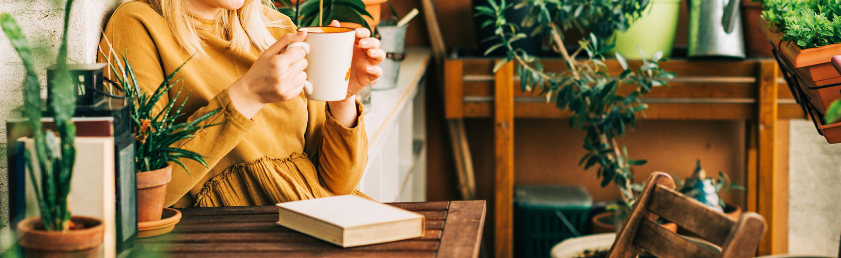 Woman sipping tea while reading a book surrounded by plants