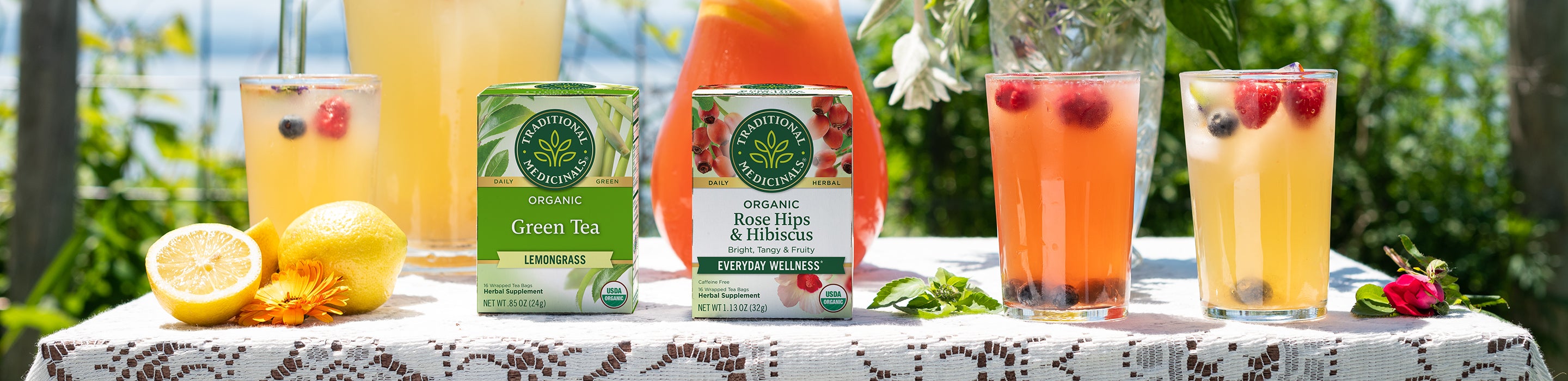 Herbal lemonade in pitchers and glasses with Green Tea Lemongrass and Rose Hips with Hibiscus cartons on table